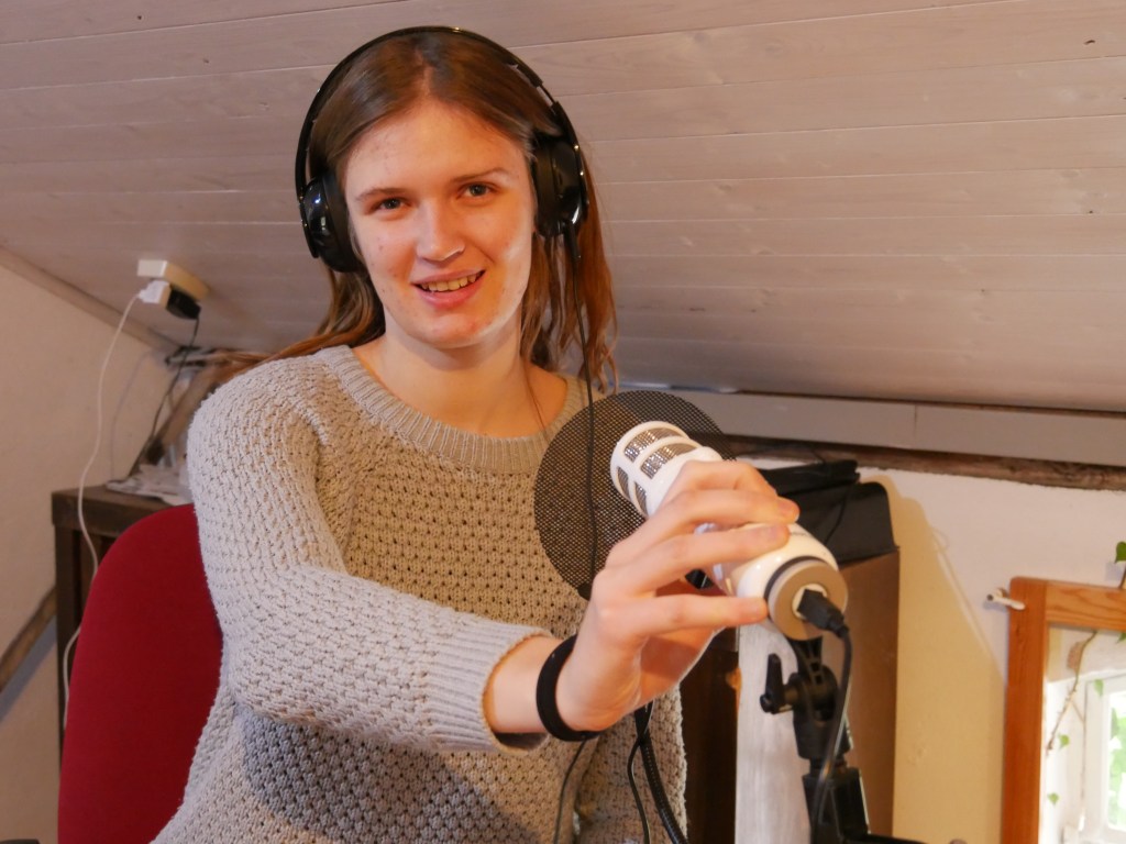 ie FSJlerin der Seefelder Mühle sitzt im Büro mit Kopfhrern und einem Mikrofon. So kann man sich eine Podcastaufnahme vorstellen